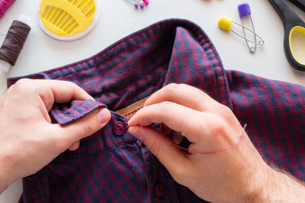 Dvě ruce přišívají knoflík na károvanou košili